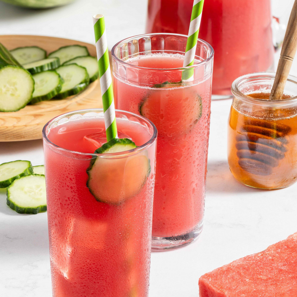 Two watermelon cucumber drinks with pitcher, fresh cucumber and fresh watermelon in the background