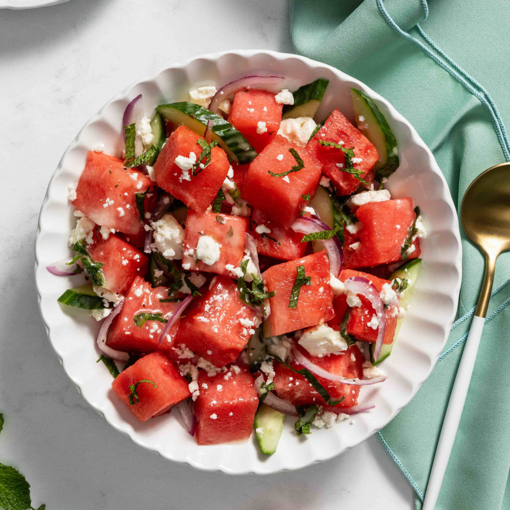 Cubed watermelon mixed with feta cheese and mint in bowl near spoon