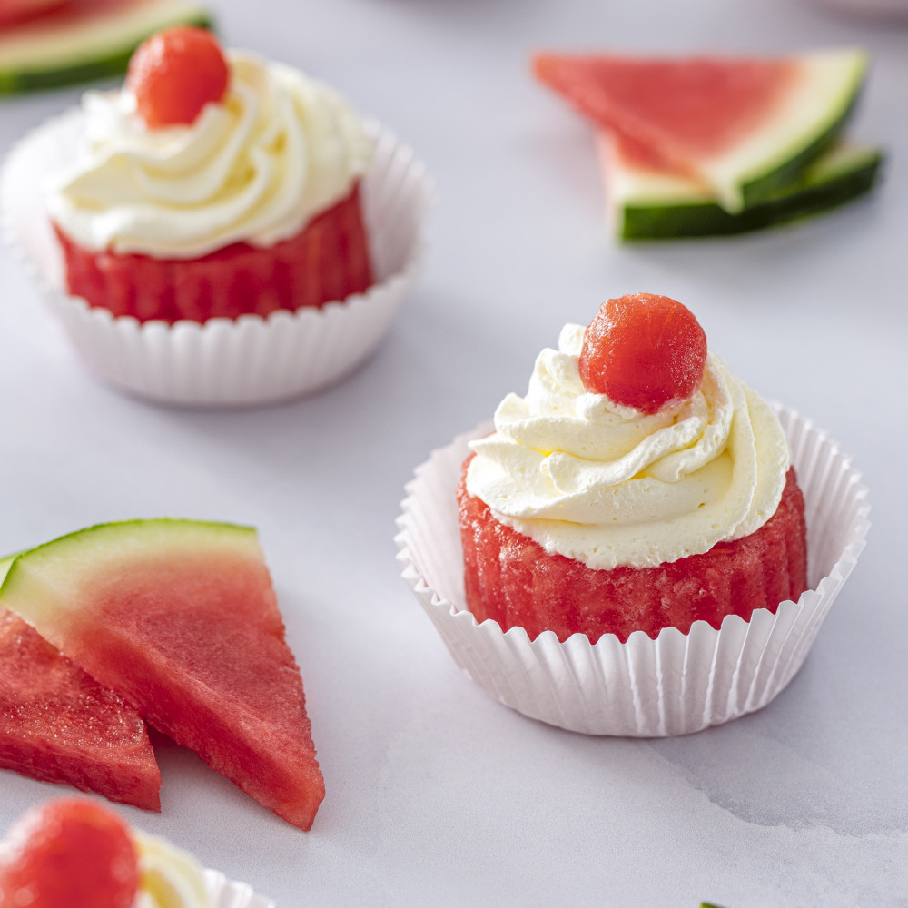 Watermelon in cupcake liners with frosting and a watermelon ball on top.