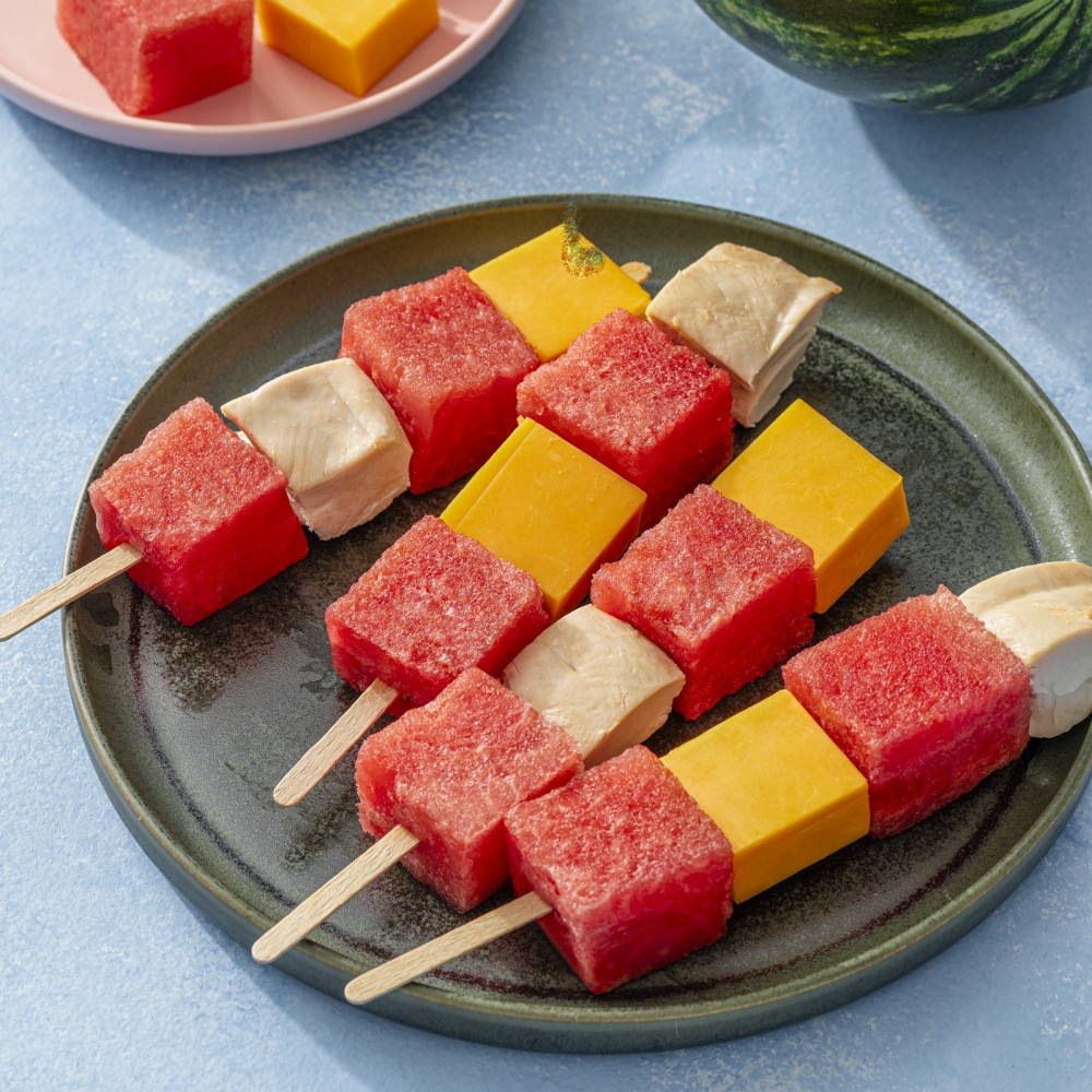 Cubed watermelon, turkey, and cheddar cheese on popsicle stick skewers on a plate.
