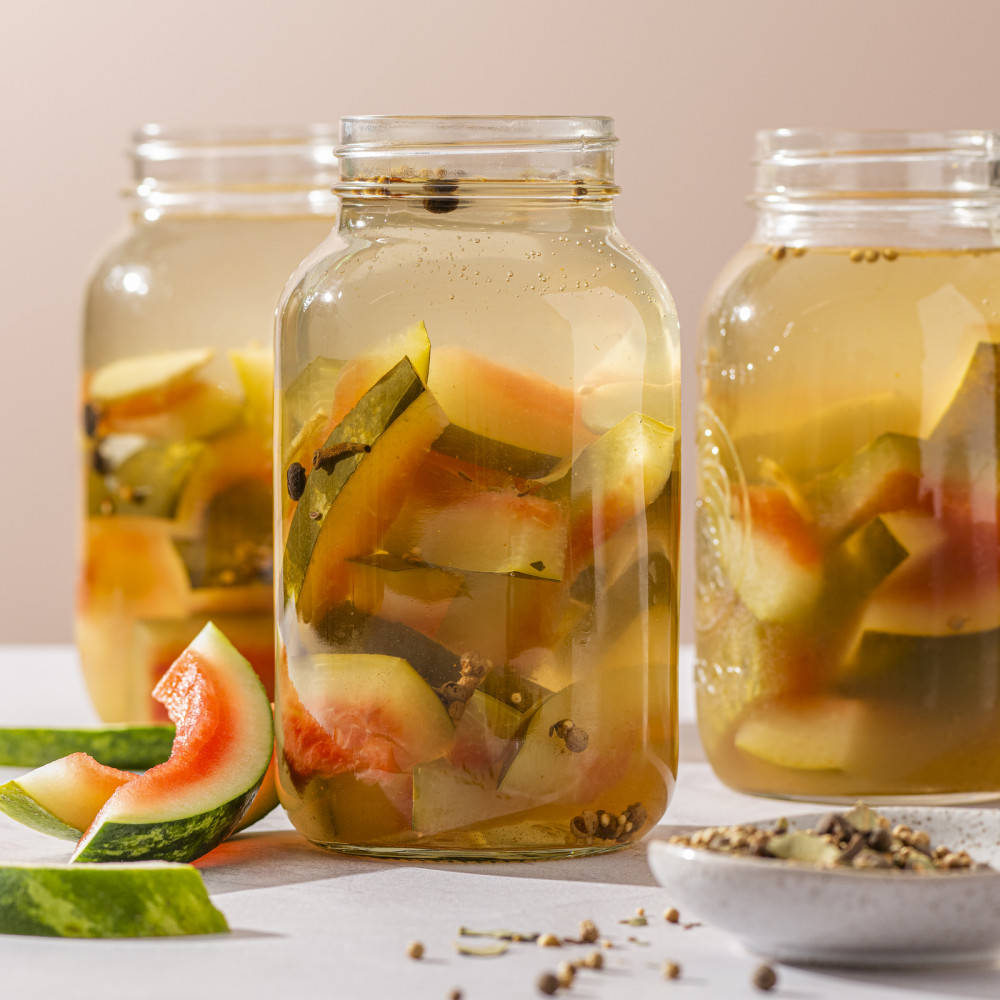 Three jars of pickles made with watermelon rind and small bowl of spices