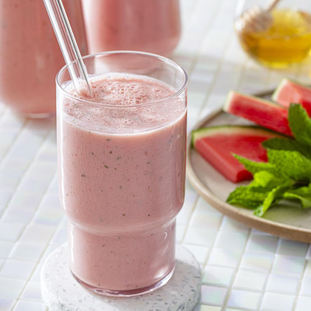 Watermelon smoothie in a clear glass with straw and a plate of watermelon wedges with mint.