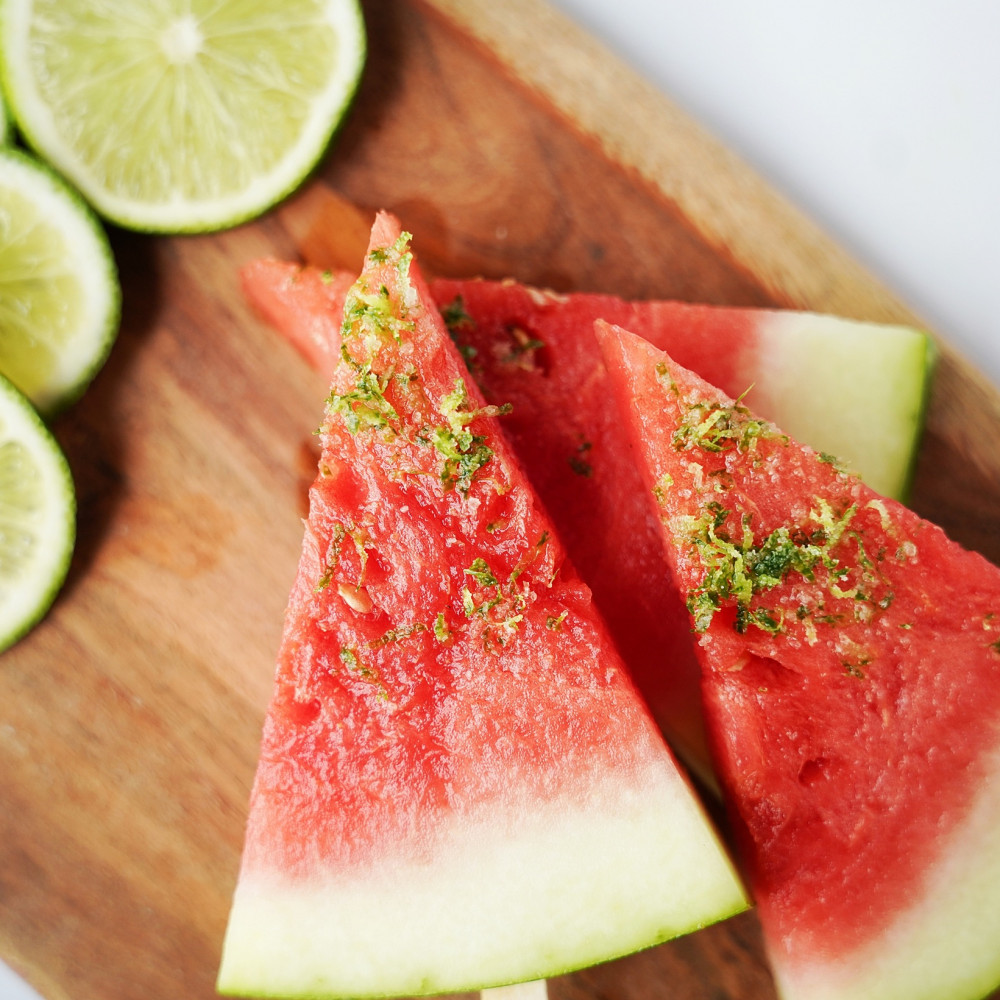 Three watermelon wedges with popsicle sticks in the rind and topped with lime shavings and salt.