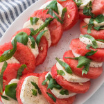 Watermelon Caprese Salad topped with basil and pepper on a platter with a blue and white striped napkin.